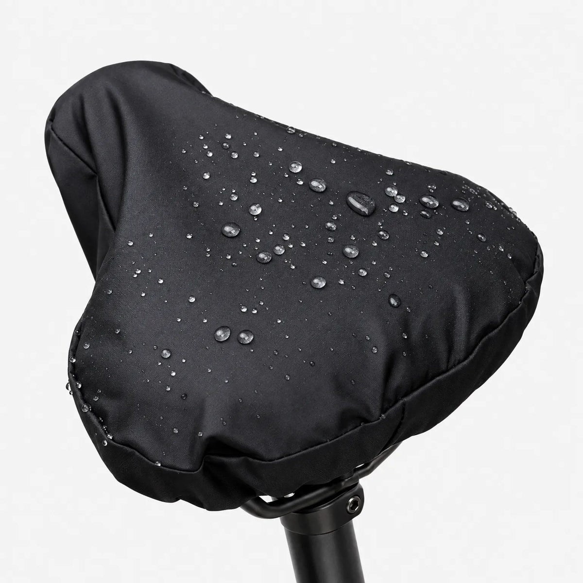 Close-up of the black side of the cover on a saddle, with raindrops sitting on the smooth fabric against a white background. 2