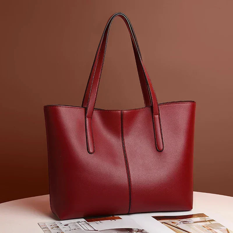 Deep red tote bag angled on a white table beside a magazine, brown backdrop 3