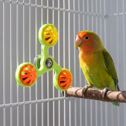 Green spinner toy with yellow and orange bell balls attached to white cage bars, while a lovebird perches on a wooden branch beside it. 3