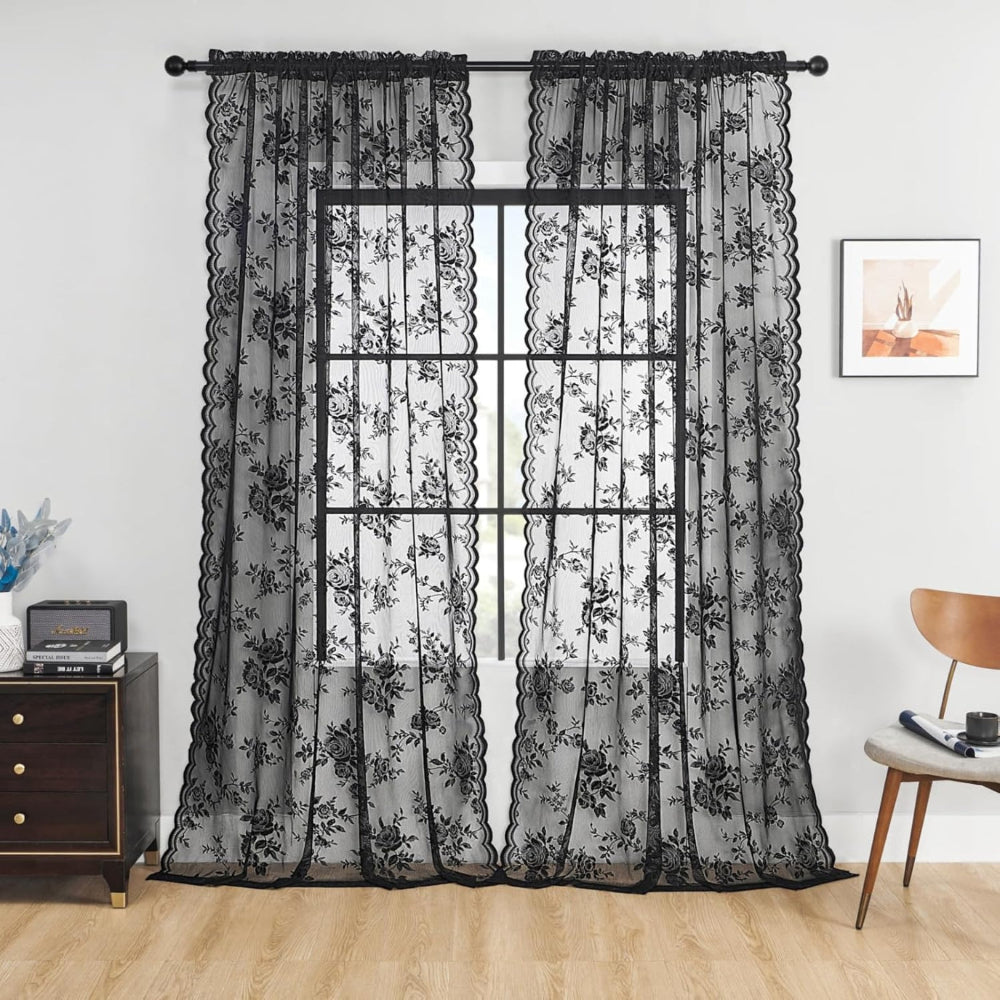 Pair of black rose lace curtain panels hung on a dark rod at a window, with scalloped edges, in a living room. 1