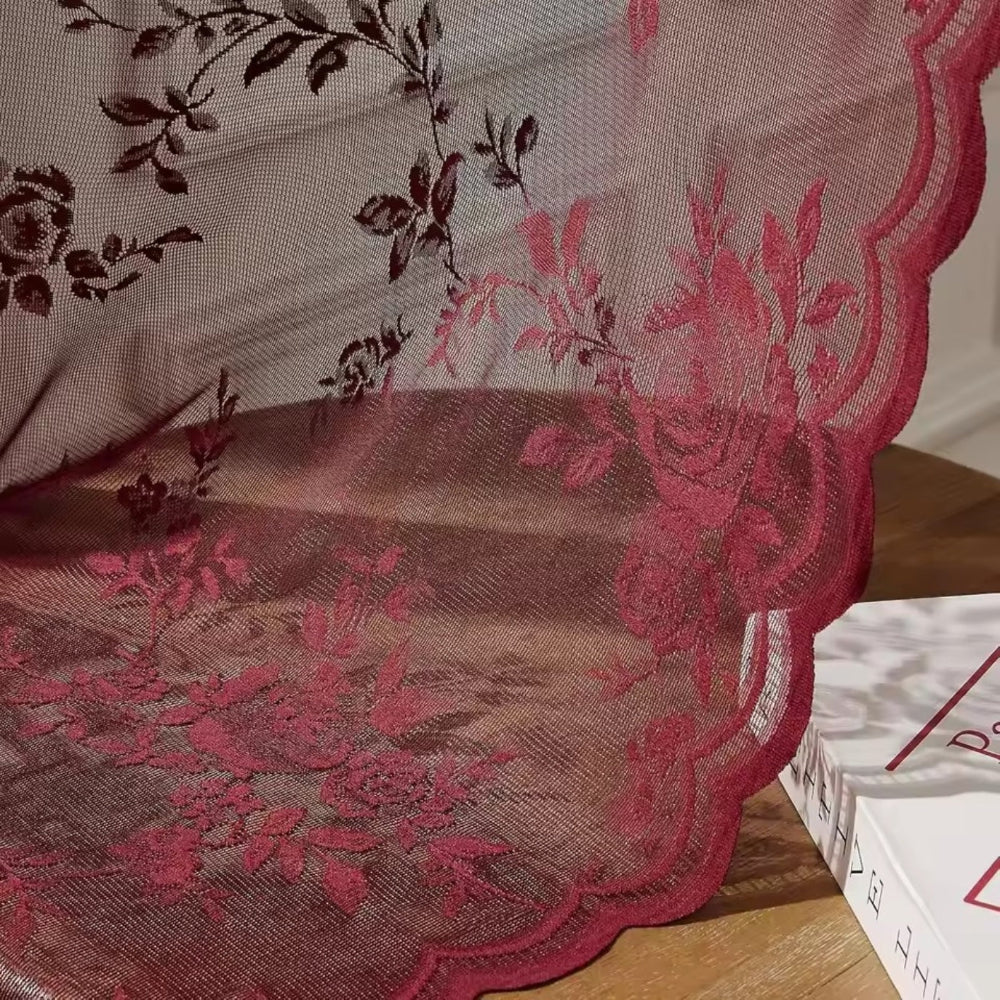 Close-up of red rose lace fabric with a scalloped edge, draping over a wooden surface beside a book. 3