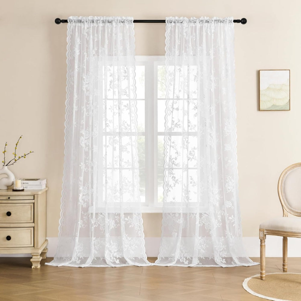 Pair of white floral lace curtain panels on a black rod in front of a window, in a cream-walled room. 6