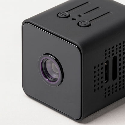 Close-up of the black cube camera from the front corner, showing the lens with a purple ring, top buttons and ventilation holes. 5
