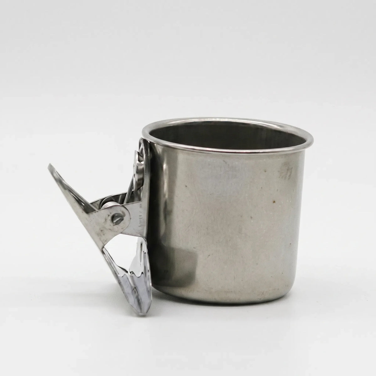 Side view of a steel cup with its spring clip held open, showing the clip's jaws. 6