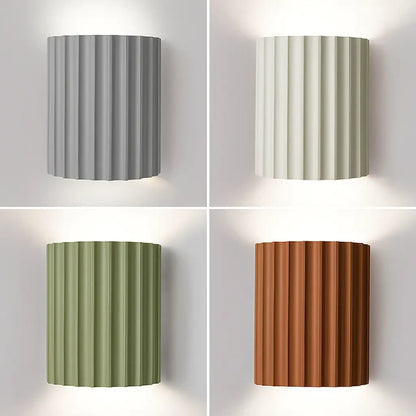 Four fluted half-cylinder wall lights in grey, cream, green and terracotta, each glowing up and down 1