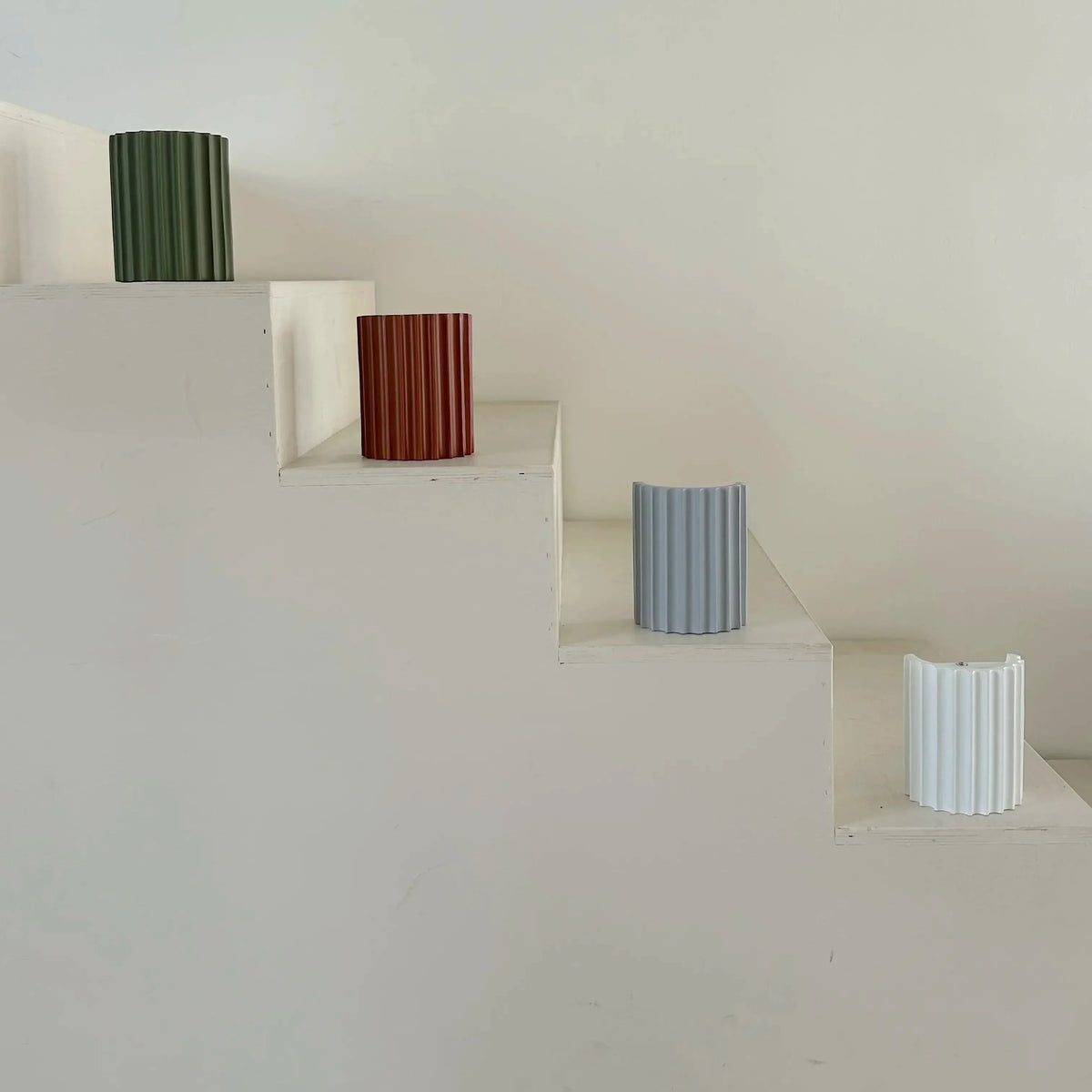 Green, terracotta, grey and white fluted lights lined up on the steps of a white wooden staircase 10