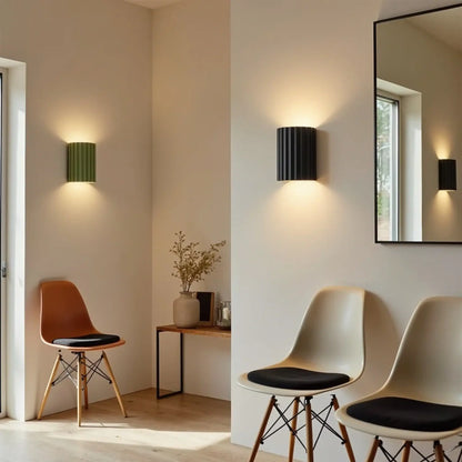 Green and black fluted wall lights glowing in a bright hallway with moulded chairs and a mirror 3