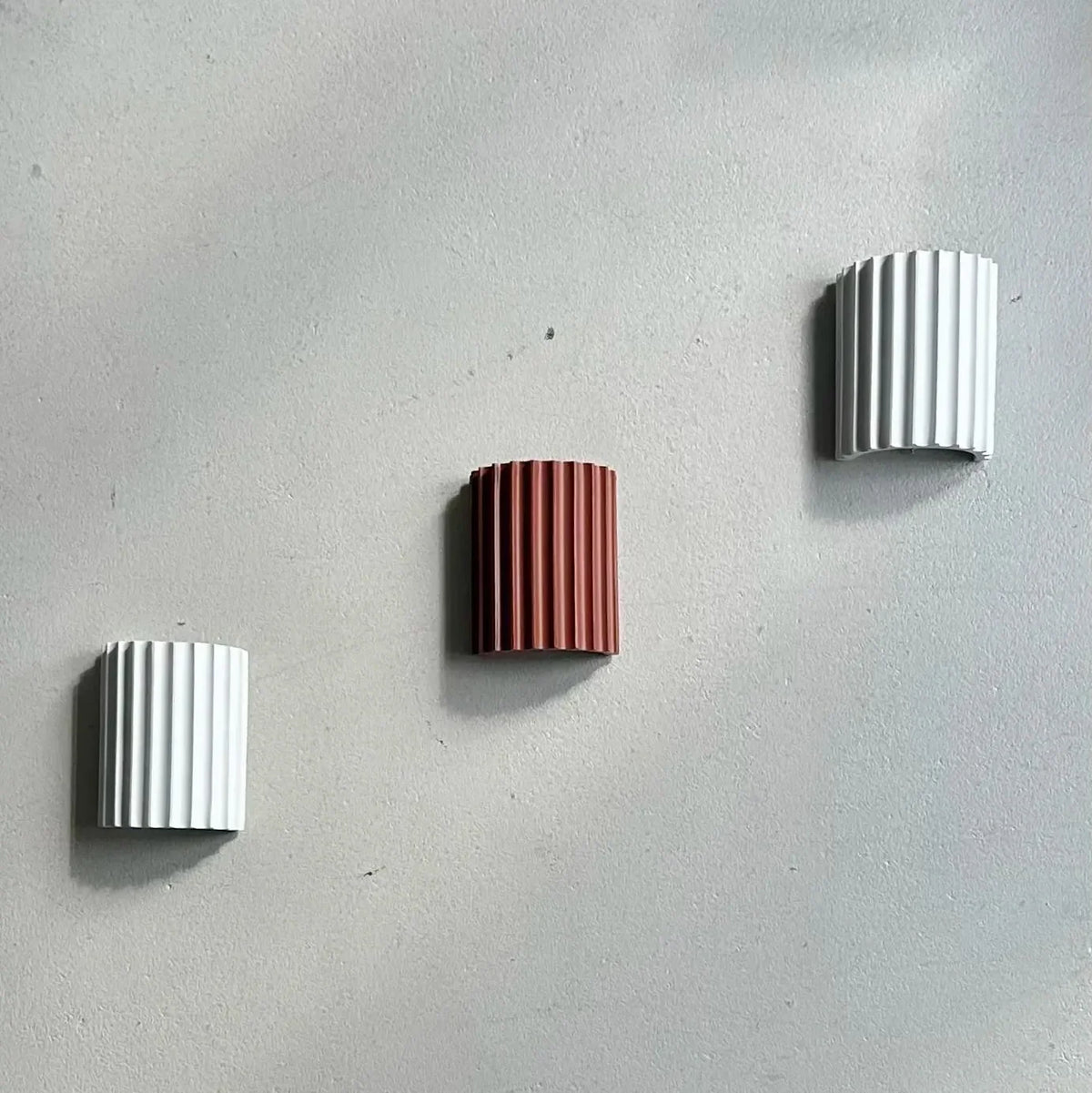 Two white and one terracotta fluted wall light mounted unlit in a diagonal line on a grey wall 13