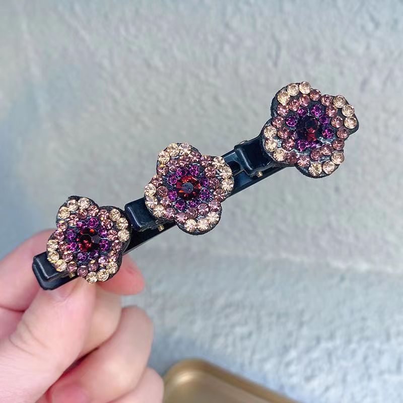 Hand holding one black hair clip with three flowers set with purple, pink and champagne rhinestones. 2
