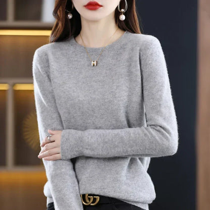 Light grey crew-neck jumper with ribbed cuffs, worn with black trousers and a belt, hands clasped in front 20