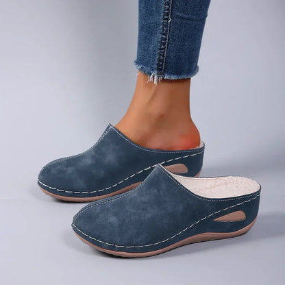 Blue backless slippers worn by a model in frayed jeans, showing the cream fleece lining and side cut-out in the sole. 4