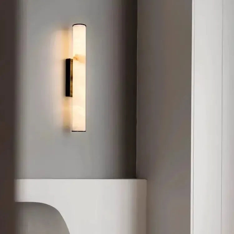 Dark-capped marble wall light glowing in a grey alcove corner above a curved white shelf, with amber veining visible near the top. 20
