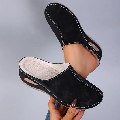 Black backless slippers lifted in one hand, one turned to show the thick fleece lining, the other worn on a foot. 5