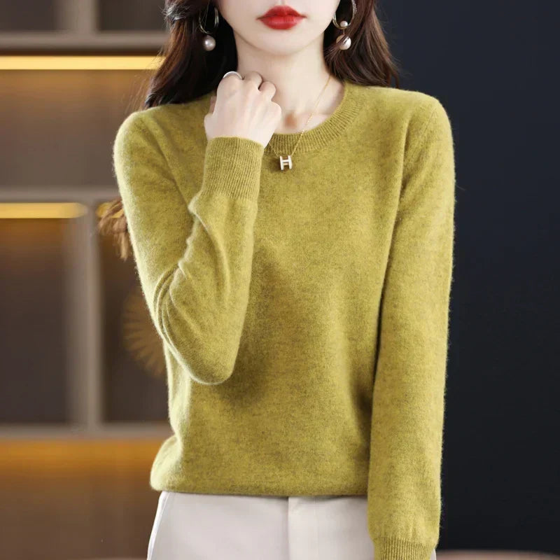 Mustard-green crew-neck jumper with ribbed collar and cuffs, model's hand raised to the collarbone 13