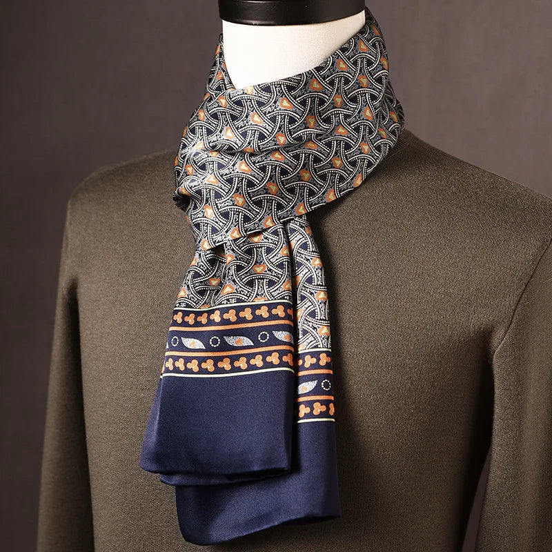 Navy silk scarf with an interlocking orange and white arc pattern and a decorative border, draped on a mannequin in an olive jumper. 11