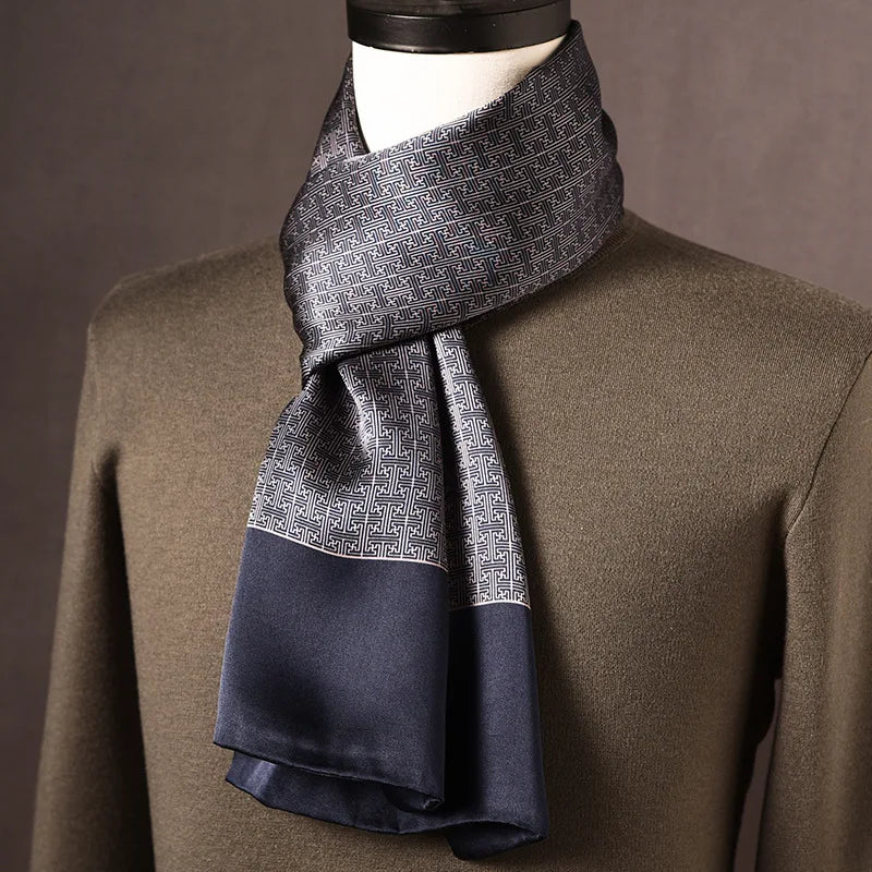 Grey and navy silk scarf with a small geometric maze-like pattern and plain navy ends, draped on a mannequin in an olive jumper. 10