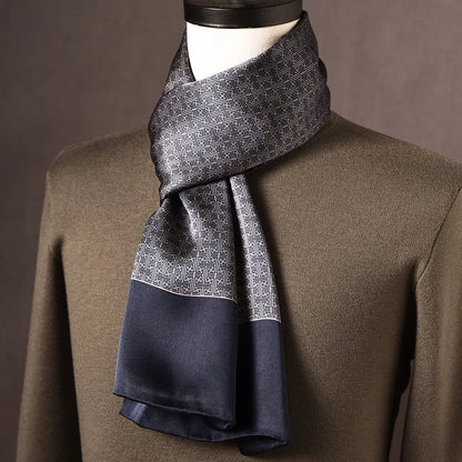 Grey and navy silk scarf with a small geometric maze-like pattern and plain navy ends, draped on a mannequin in an olive jumper. 10