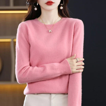 Pink crew-neck jumper with ribbed cuffs, worn with cream trousers and one arm folded across the body 10