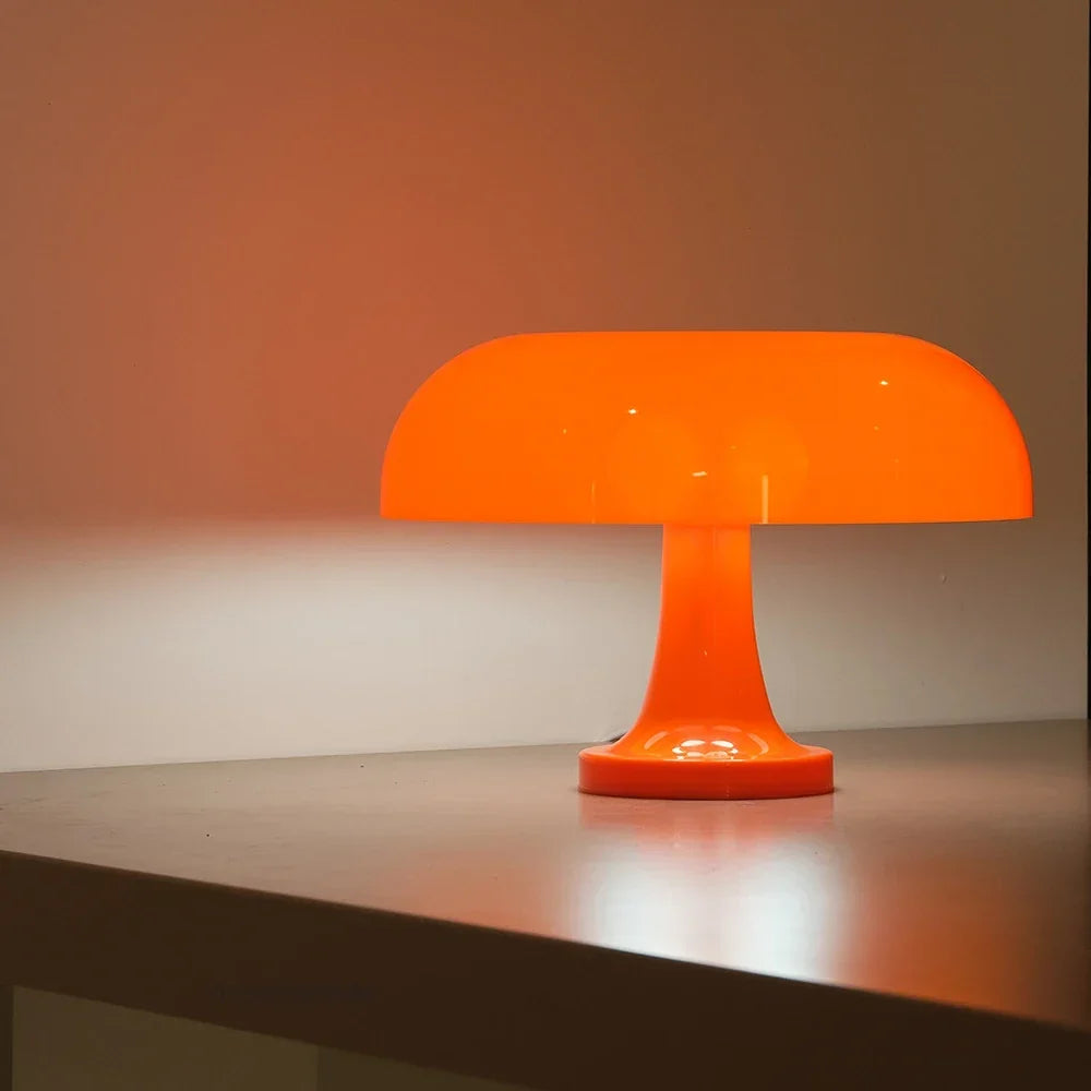 Orange lamp lit on a shelf edge against a warm orange-washed wall, showing the shade and flared stem in profile. 6