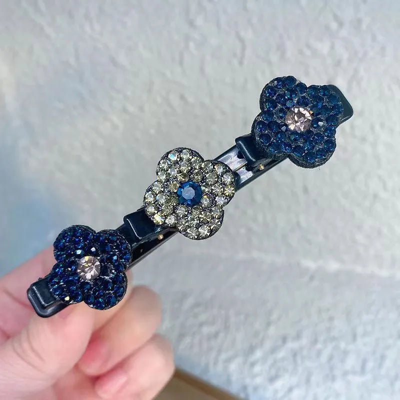 Hand holding one black clip with three rhinestone flowers, two deep blue and a central one in grey with a blue centre. 3