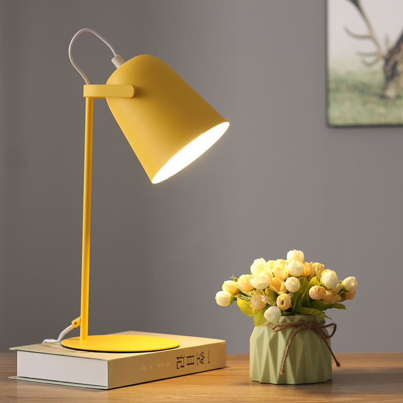 Lit yellow lamp on a stack of books beside a vase of roses, with a framed picture behind. 7