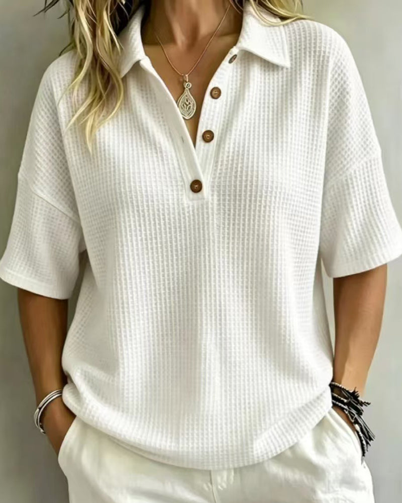 Model wearing the white waffle knit polo top with three wooden buttons, hands in pockets, front view 1