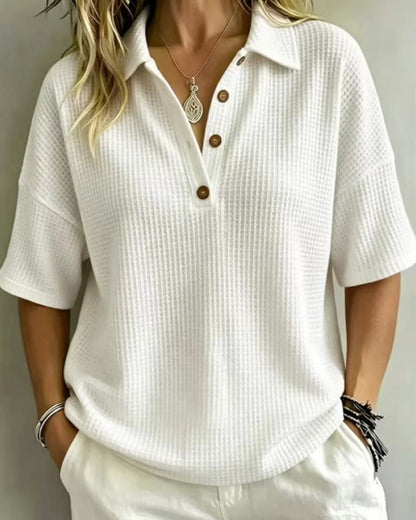 Model wearing the white waffle knit polo top with three wooden buttons, hands in pockets, front view 1
