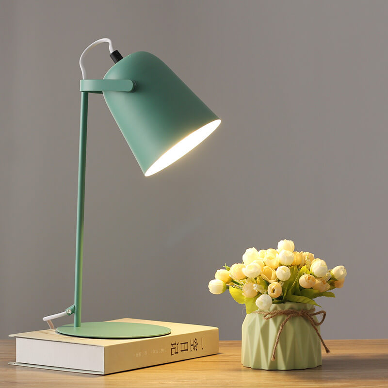 Green version of the lamp glowing warmly on a book beside a small vase of artificial flowers. 9