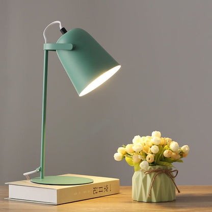 Green version of the lamp glowing warmly on a book beside a small vase of artificial flowers. 9
