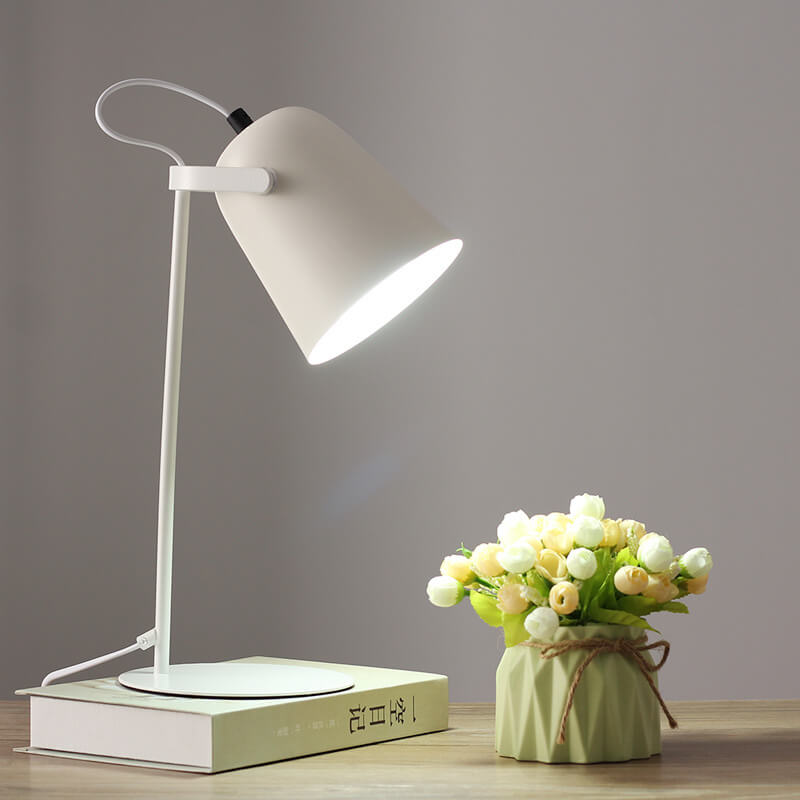 White version of the lamp switched on, set on a book next to a vase of cream flowers. 11