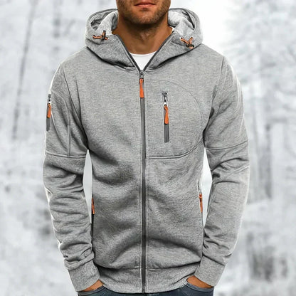 Model wearing the hoodie in light grey with a textured jacquard finish and orange zip pulls, snowy backdrop. 8