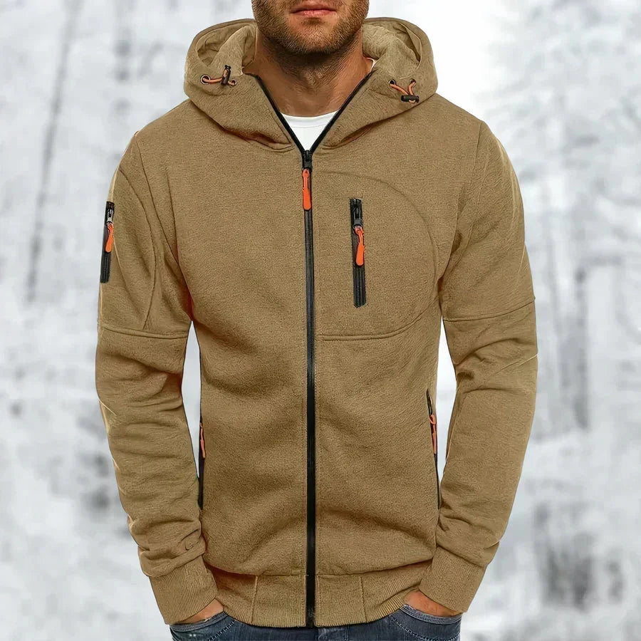 Model wearing the hoodie in camel brown with orange zip pulls, a black front zip and ribbed hem, snowy backdrop. 10