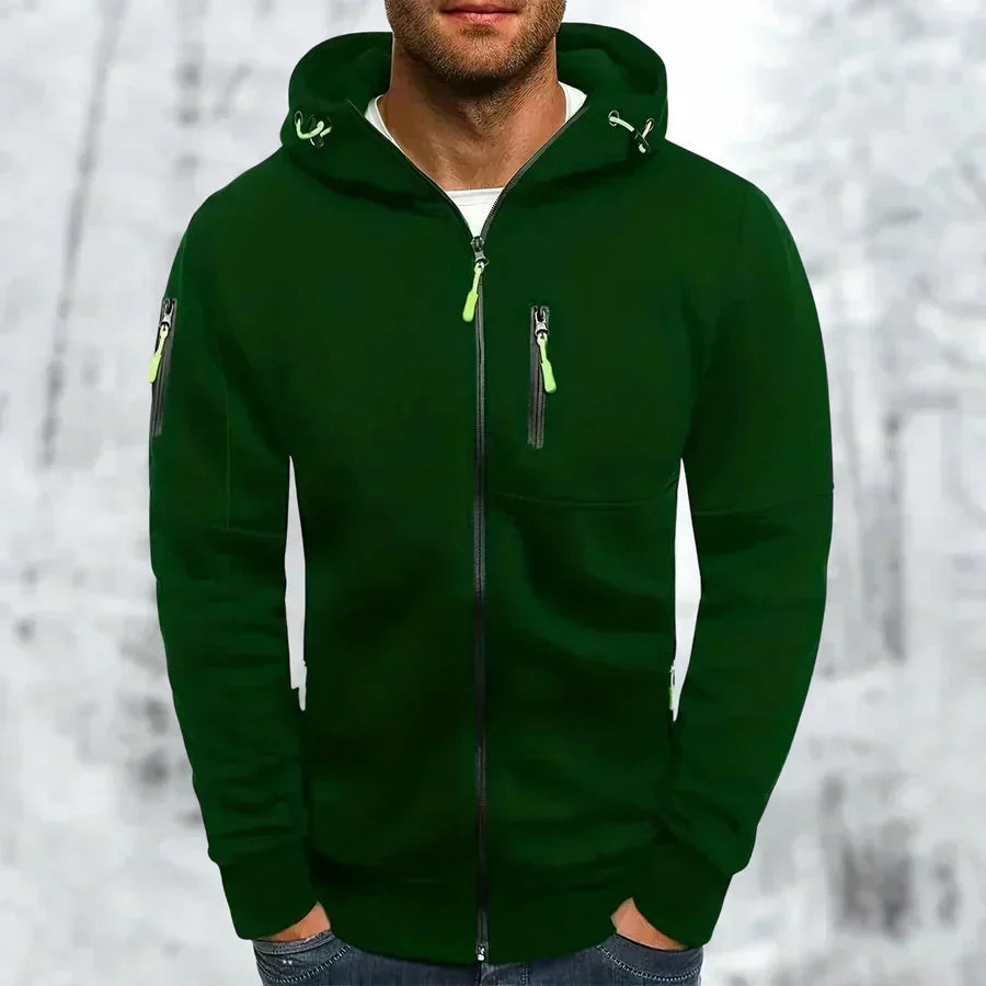 Model wearing the hoodie in dark green with lime green zip pulls and drawcords, hands in jeans pockets, snowy backdrop. 6