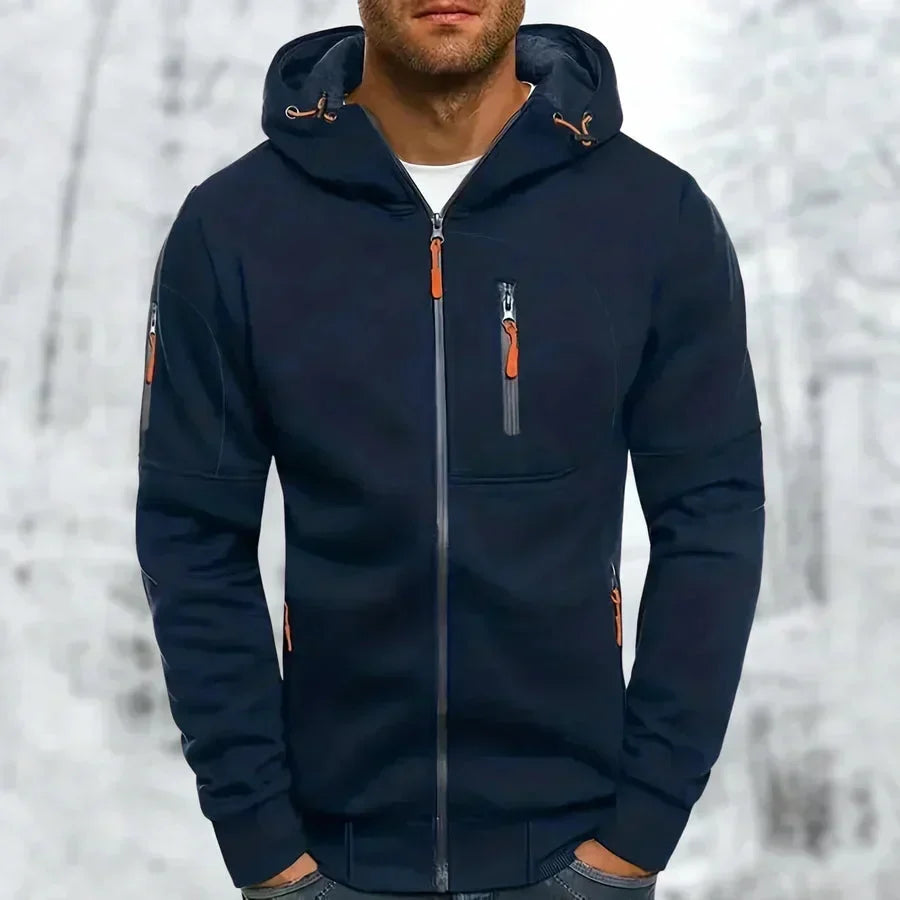 Model wearing the hoodie in navy blue with orange zip pulls and a chest zip pocket, snowy backdrop behind. 5
