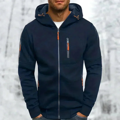 Model wearing the hoodie in navy blue with orange zip pulls and a chest zip pocket, snowy backdrop behind. 5