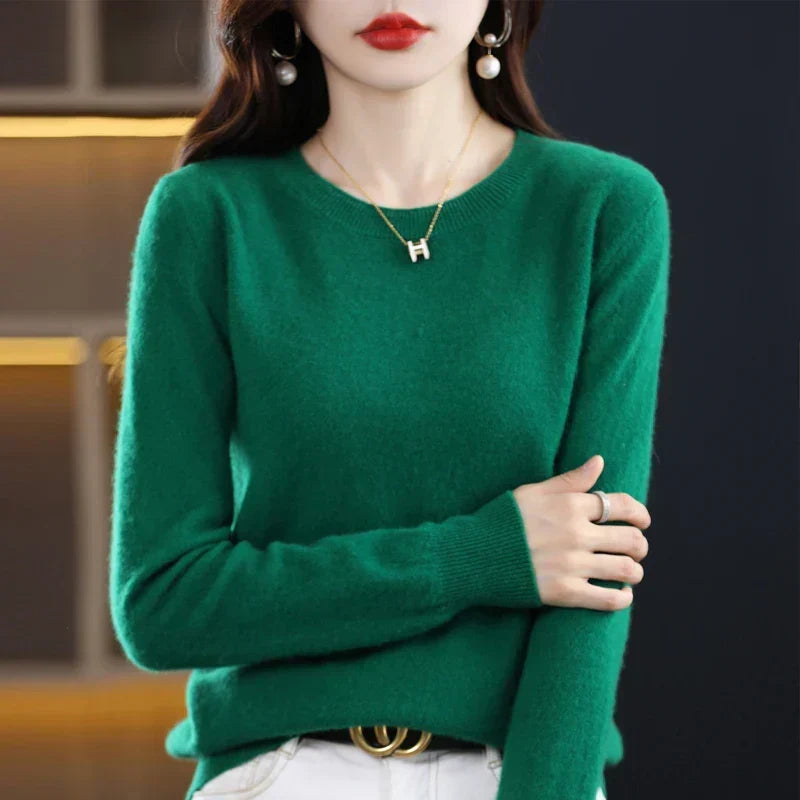 Emerald-green crew-neck jumper worn with white trousers and a belt, one arm folded across the body 6