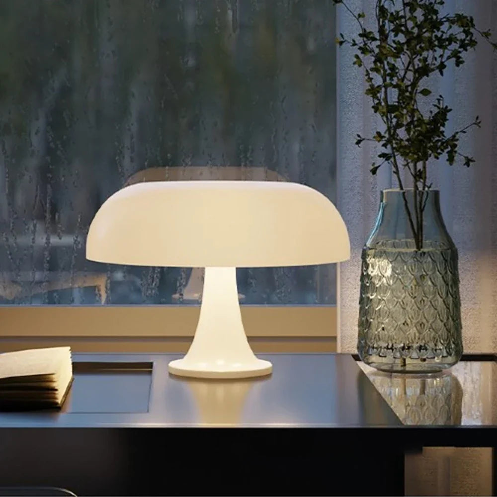 White lamp lit on a dark desk beside an open book and a textured glass vase, with a rain-streaked window behind. 4