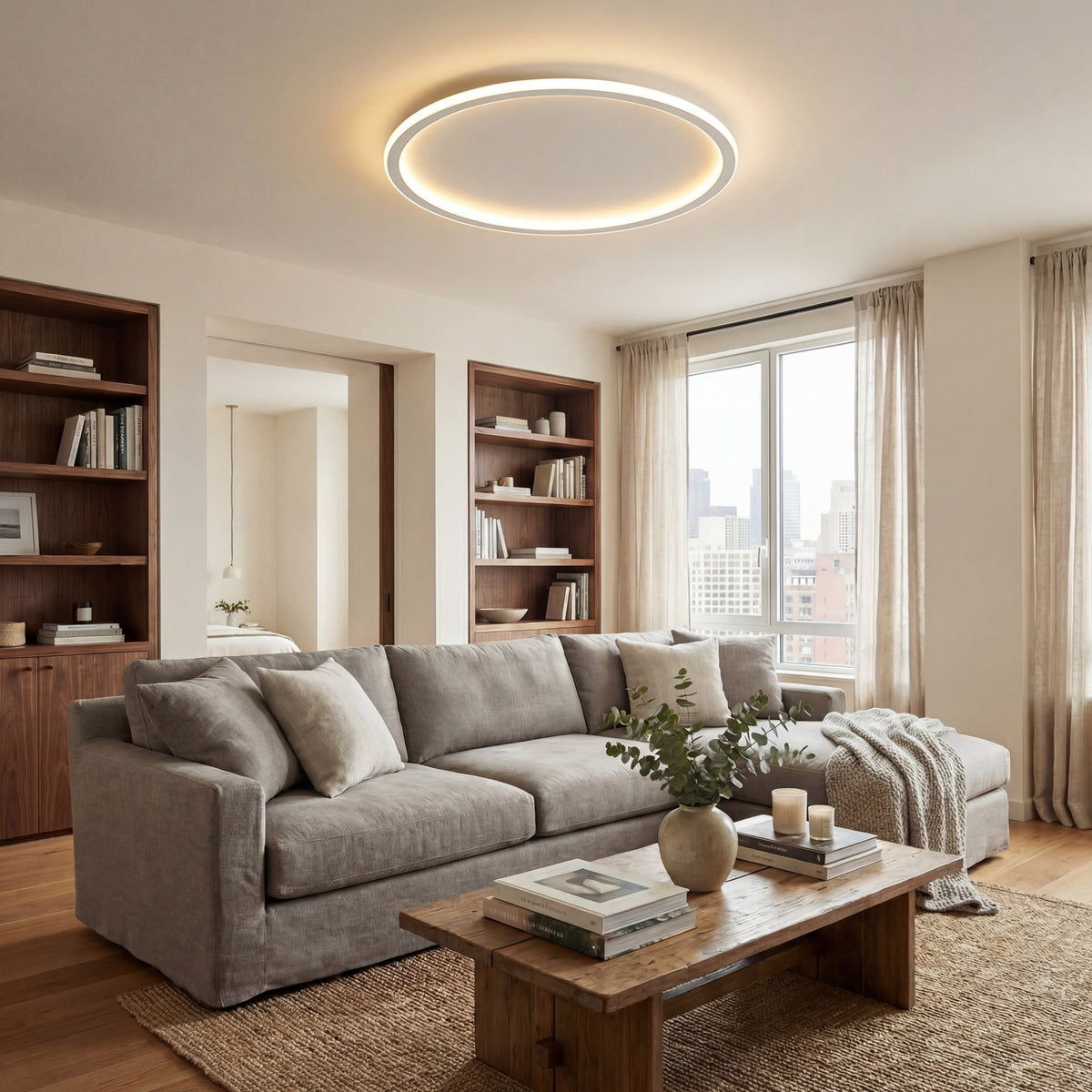 Large ring ceiling light above a living room with a grey corner sofa, wooden coffee table, bookshelves and tall window. 5