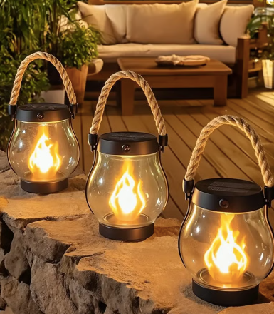 Three glowing flame-effect lanterns with rope handles standing on a stone ledge by a patio sofa 1