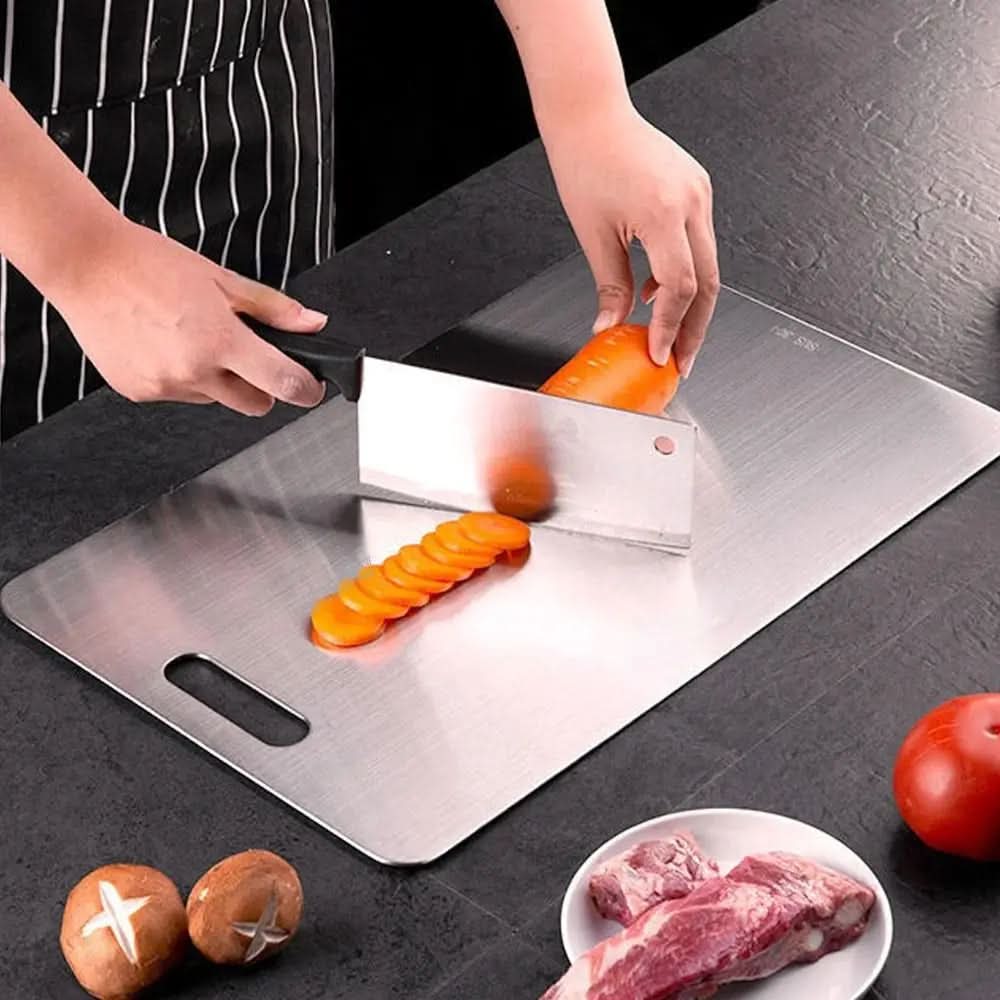 Cleaver slicing a carrot into rounds on the brushed metal board, with mushrooms, a tomato and raw meat nearby. 3