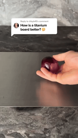 Hand holding a red onion above a smooth dark metal board on a marble worktop, with a video comment overlay. 5