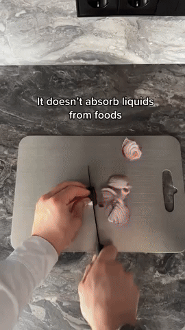 Hands cutting a colourful food item on a grey board with a handle slot, on a marble surface. 7