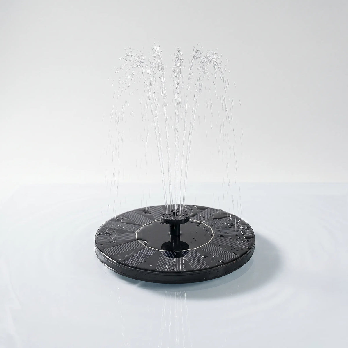 Round black solar fountain floating on calm water, spraying a fan of fine jets from its central nozzle against a plain pale backdrop. 1