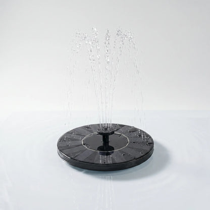 Round black solar fountain floating on calm water, spraying a fan of fine jets from its central nozzle against a plain pale backdrop. 1