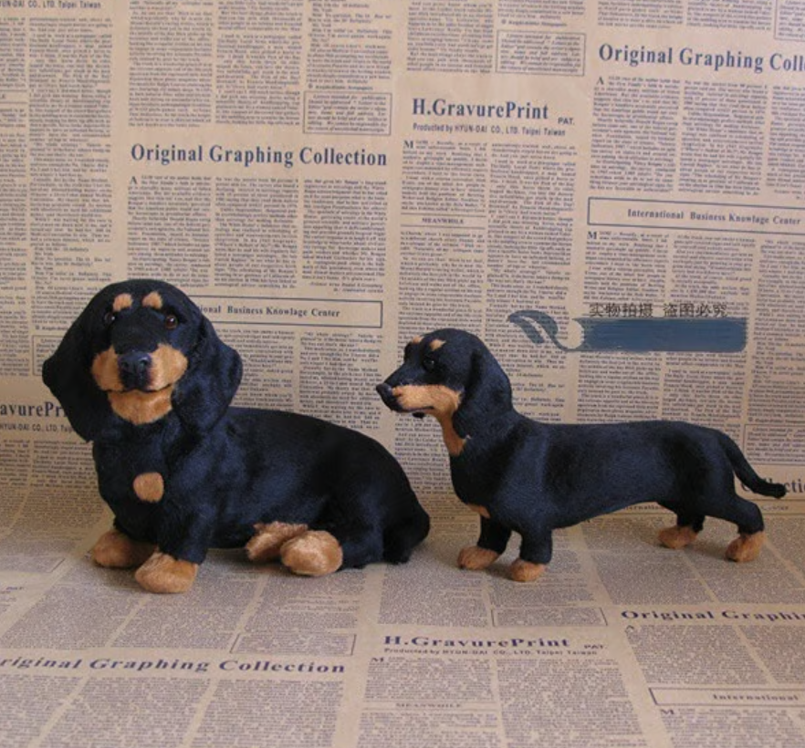 Two plush dachshunds, one black and tan sitting and one standing, shown side by side against a newspaper-print backdrop. 2