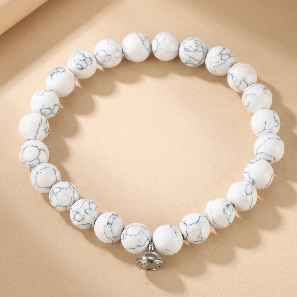 White beaded bracelet with fine grey veining and a silver-tone magnetic charm, on a beige background 3