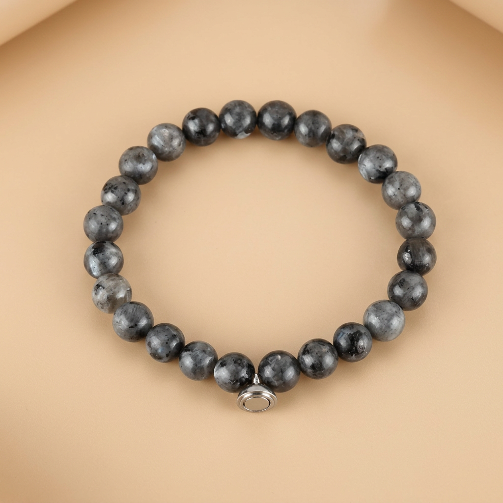 Grey speckled stone bead bracelet with a silver-tone magnetic charm, laid flat on a peach background 4