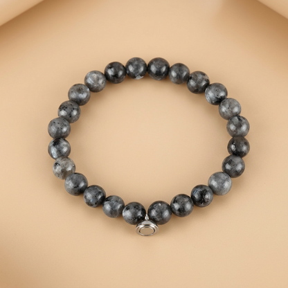 Grey speckled stone bead bracelet with a silver-tone magnetic charm, laid flat on a peach background 4