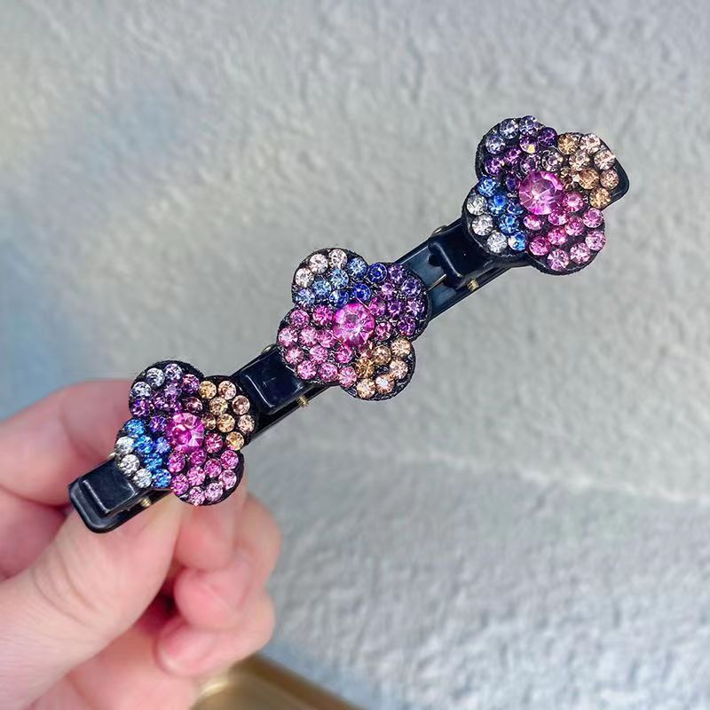 Hand holding one black clip with three multicoloured rhinestone flowers in pink, purple, blue, silver and gold tones. 5