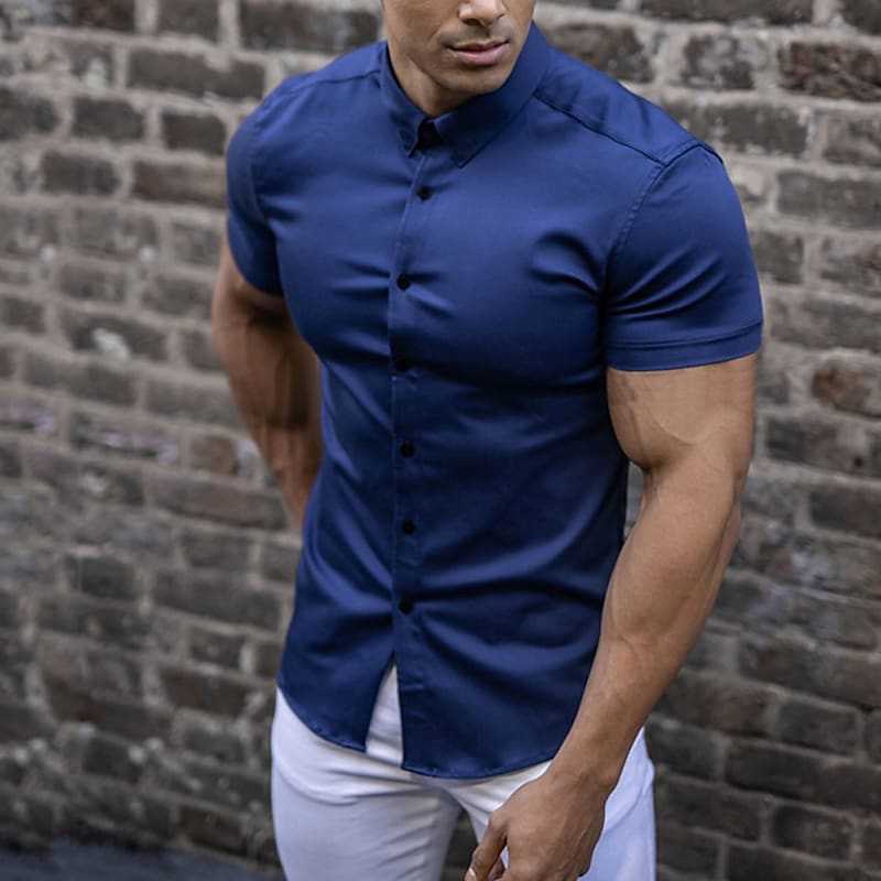 Navy blue short sleeve shirt with dark buttons, worn tucked into white trousers in front of a brick wall. 3